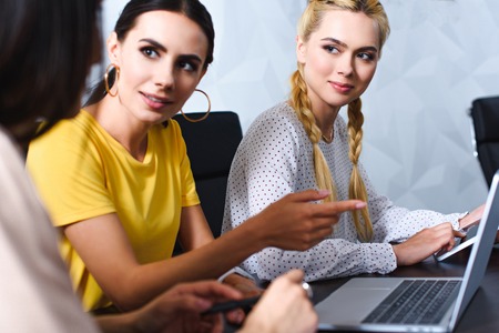 businesswoman pointing by finger at laptop screen to colleague in modern officeの写真素材