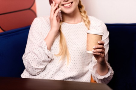 cropped shot of smiling businesswoman talking on smartphone and drinking coffee in officeの写真素材