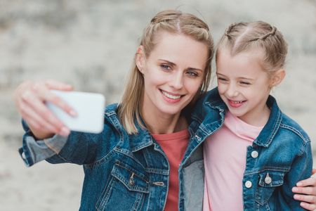 beautiful mother and daughter taking selfie on smartphoneの写真素材