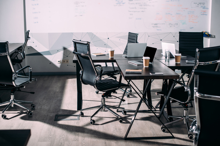 front view of interior of modern office with chairs, paper cups of coffee, laptops on tableの写真素材
