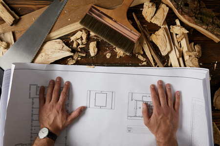 cropped shot of architect hands on blueprint at table with paintbrush, handsaw and wooden chips on tableの写真素材