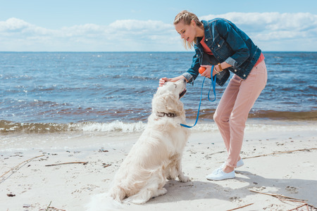 happy woman playing ball with golden retriever on sea shore