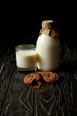 close up view of chocolate cookies, fresh milk in glass and bottle wrapped by paper on black backgroundの写真素材