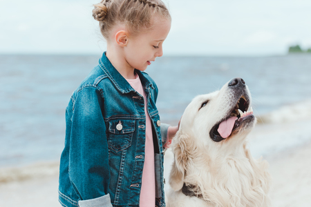 adorable child with friendly golden retriever dog on sea shoreの写真素材