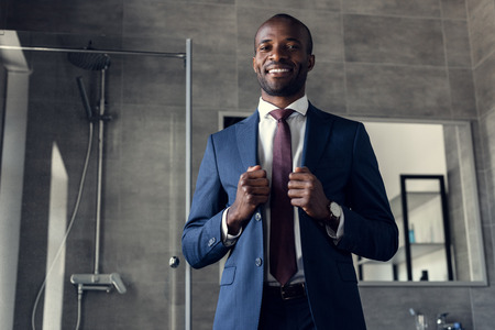 handsome young businessman in stylish suit standing in bathroom and looking at cameraの写真素材