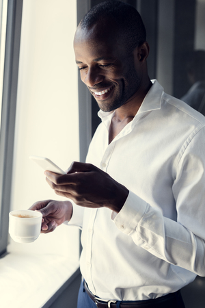 smiling young businessman in white shirt using smartphone during coffee breakの写真素材
