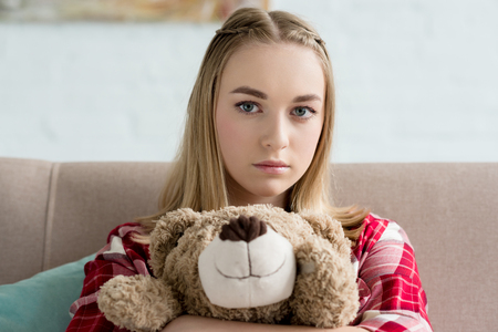 close-up portrait of beautiful teen girl embracing her teddy bear and looking at cameraの写真素材