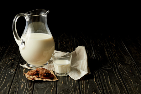 closeup view of fresh milk in jug and glass, chocolate cookies and sackcloth on black backgroundの写真素材