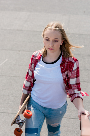 beautiful teen girl in red plaid shirt walking with skateboard in handの写真素材