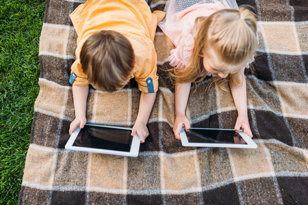 overhead view of cute little kids using digital tablets while lying on plaidの写真素材