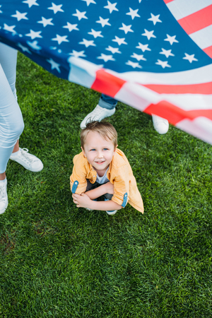 cropped shot of parents holding american flag and little son crouching on grassの写真素材