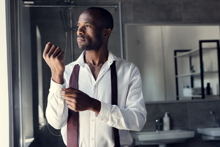thoughtful young businessman in white shirt buttoning cufflinks and looking awayの写真素材