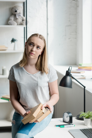 thoughtful teen student girl with books sitting on work desk at homeの写真素材