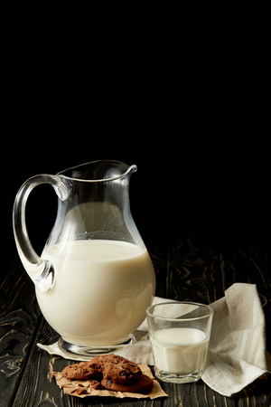 fresh milk in jug and glass, chocolate cookies and sackcloth on black backgroundの写真素材