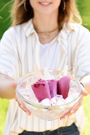 Woman holding bowl with berry popsicles and ice cubes