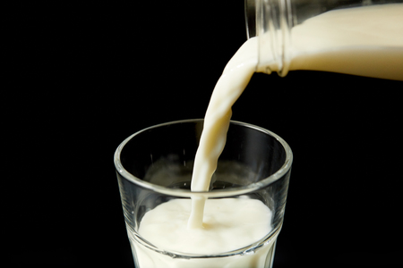 closeup view of milk pouring into glass from bottle isolated on blue backgroundの写真素材