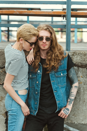 boyfriend with tattoos and stylish girlfriend posing in sunglasses near bridgeの写真素材