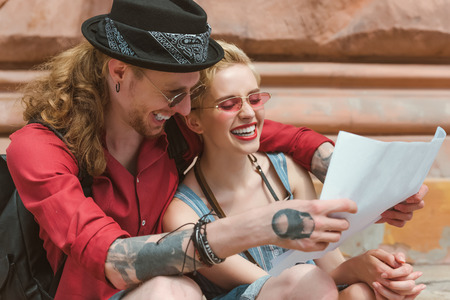 couple of young tourists laughing and looking at map in cityの写真素材