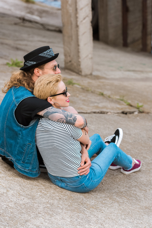 side view of boyfriend with tattoos hugging stylish girlfriend and they looking awayの写真素材