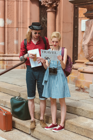 couple of tourists with coffee reading travel newspaper while standing on stairs with retro suitcasesの写真素材
