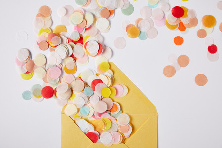 top view of colored confetti pieces and yellow envelope on white surfaceの写真素材