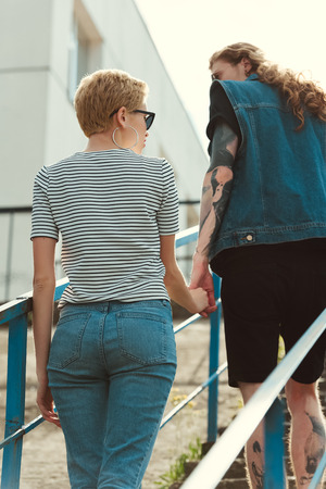 back view of boyfriend with tattoos and stylish girlfriend holding hands and walking on stairsの写真素材