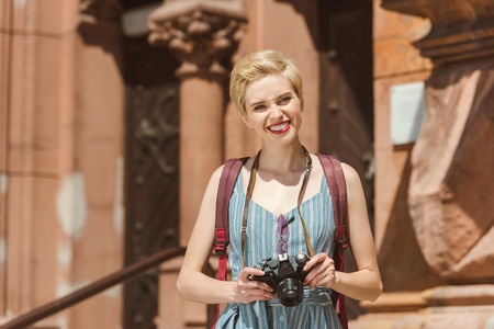 smiling traveler with backpack and photo camera in cityの写真素材