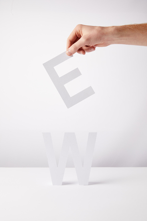 cropped view of person holding paper letters - e and w, on white backgroundの写真素材