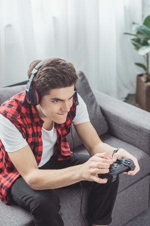 teen boy with headset playing video game with joystick at homeの写真素材