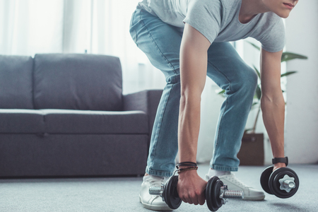 cropped view of teen boy squatting with dumbbells at homeの写真素材