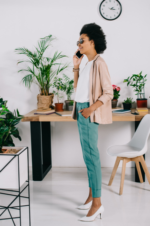side view of attractive african american businesswoman talking by smartphone in officeの写真素材