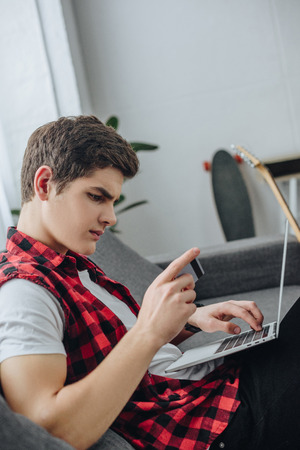 teenager using laptop and credit card at homeの写真素材