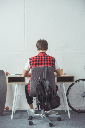 back view of male student doing homework at tableの写真素材