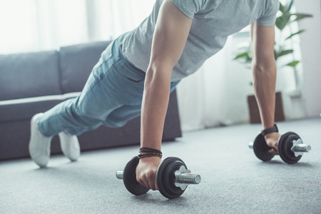 partial view of young man doing push ups with dumbbells at home