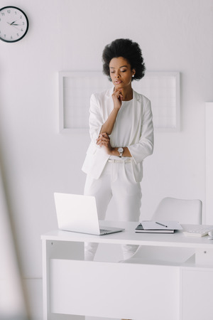 pensive attractive african american businesswoman looking at laptop in officeの写真素材