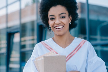 smiling attractive african american businesswoman standing with books on streetの写真素材