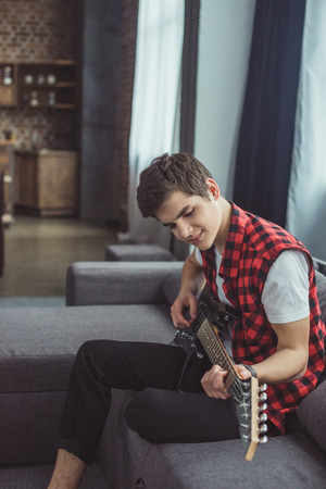 smiling teenager playing electric guitar at homeの写真素材