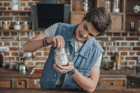 smiling teenager taking dollar banknotes from saving glass jar for moneyの写真素材