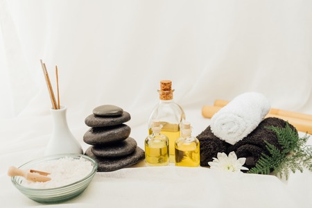 close up view of arrangement of spa treatment accessories with towels, pebbles and essential oil on...