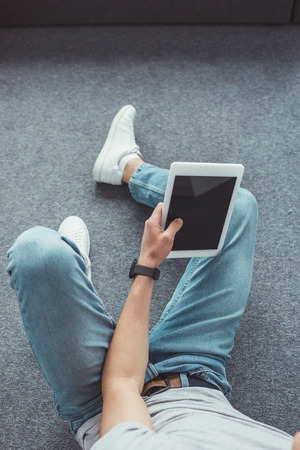 cropped view of young man using tablet with blank screen while sitting on floorの写真素材