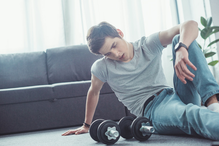 young tired boy sitting on floor after training with dumbbellsの写真素材