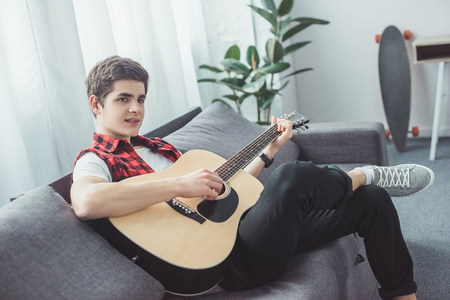 youth teenager playing acoustic guitar on sofaの写真素材