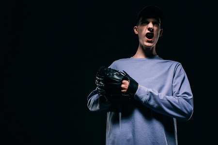 Screaming young man with baseball glove isolated on black