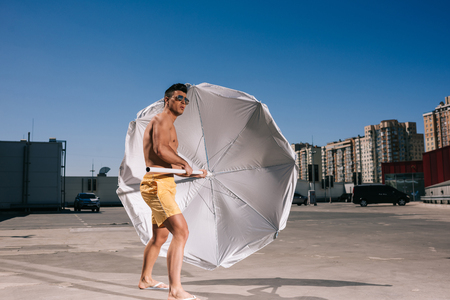 attractive young shirtless man with beach umbrella on parkingの写真素材