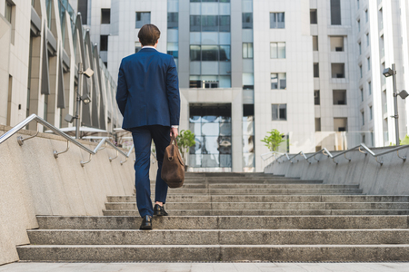 rear view of businessman in stylish suit with leather briefcase going up stairsの写真素材