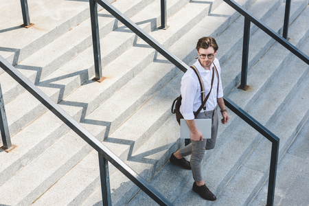 high angle view of handsome young man walking on stairs with laptop on city streetの写真素材