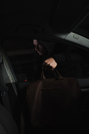 cautious male thief in black hoodie stealing bag from carの写真素材