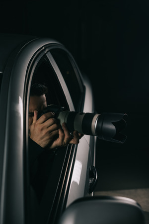 concentrated male paparazzi spying by camera with lens from his carの写真素材