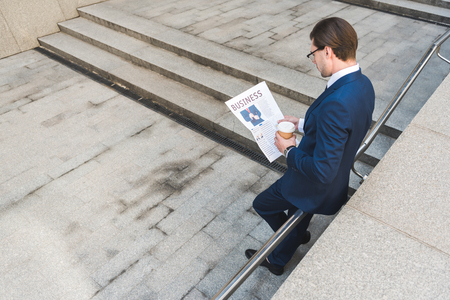 high angle view of young businessman with coffee to go reading newspaperの写真素材