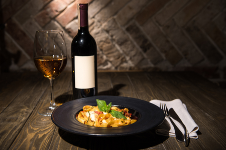 close up view of fettuccine pasta, wine and cutlery on napkin on wooden tabletopの写真素材